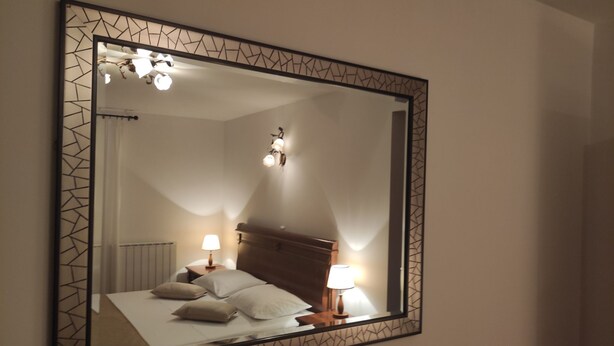 A bedroom with a large mirror, a bed with pillows, two bedside lamps, and a ceiling light fixture. - Große Wohnung in Gabonjin mit Großem Garten by Interhome (Krk/Milohnići)