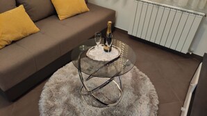 A living room with a brown sofa, two yellow cushions, a glass coffee table with a tray, a bottle of champagne, and a fluffy rug. - Große Wohnung in Gabonjin mit Großem Garten by Interhome (Krk/Milohnići)