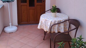 A small patio with a round table, two wicker chairs, a green umbrella, and a potted plant. - Große Wohnung in Gabonjin mit Großem Garten by Interhome (Krk/Milohnići)