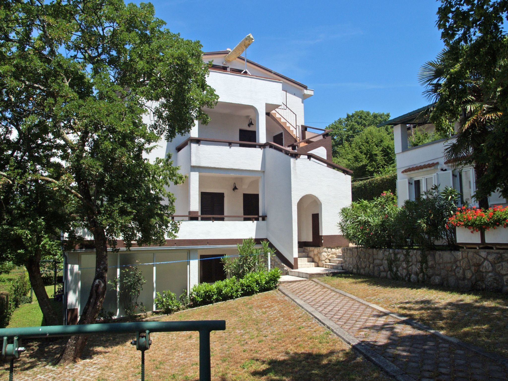 A two-story building with a white facade, a stone wall, and a paved pathway leading to the entrance.