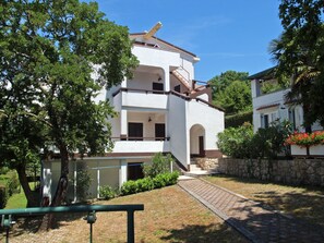 Ein zweigeschossiges Gebäude mit weißer Fassade, einer Steinmauer und einem gepflasterten Weg zum Eingang.