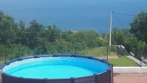 En rund pool som står ovan jord, med utsikt över havet och grönskan i bakgrunden.