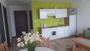 Een kleine keuken met witte kastjes, een spoelbak en een fornuis. Er staat een eettafel met stoelen en een bloevas.