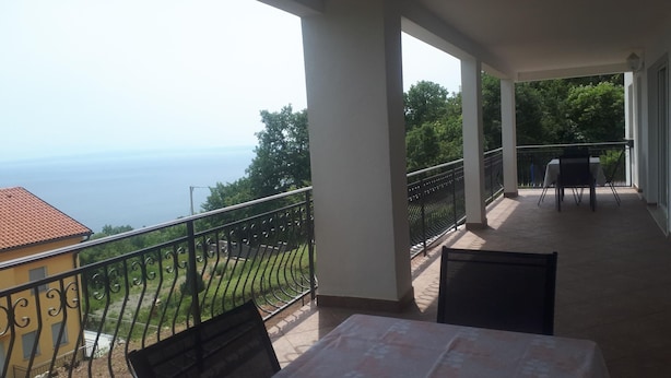 Een balkon met een tafel en stoelen, met uitzicht op een prachtig zeegezicht en groen.