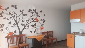 Een moderne keuken met oranje kastjes, een witte koelkast en een eethoek met een tafel en stoelen.