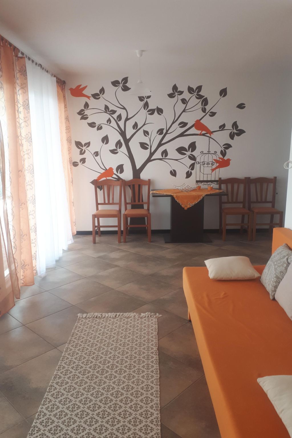 Une pièce comprenant un canapé, deux fauteuils, une table recouverte d’une nappe et un mur orné d’une fresque représentant un arbre.