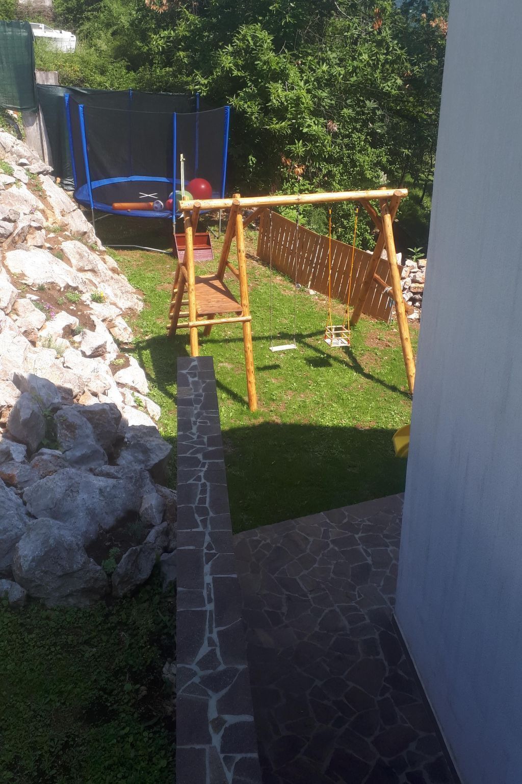 A backyard with a trampoline, a swing set, and a stone pathway.