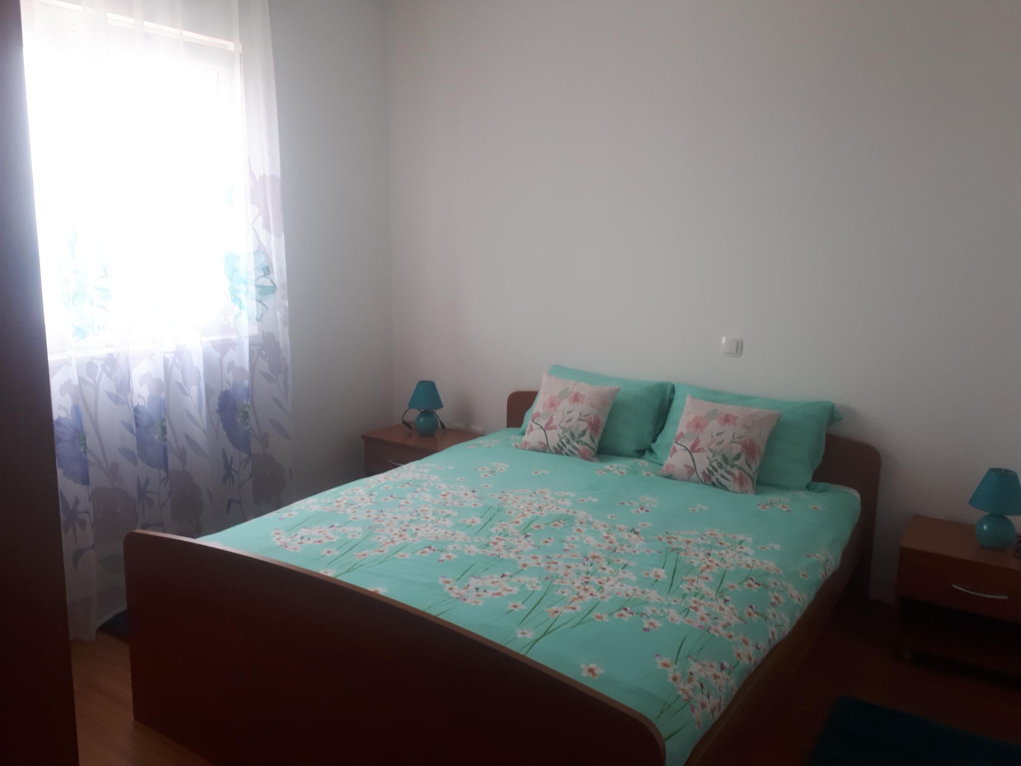 A bedroom with a bed, two bedside tables, and a window with floral curtains.