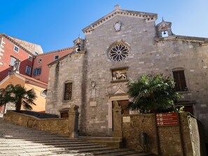 A historic stone building with a bell tower, a large circular window, and a staircase leading up to the entrance.
