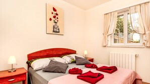 Ein Schlafzimmer mit Bett, Nachttischen, einem Fenster mit Vorhängen, einer Heizung und einem Bild an der Wand.