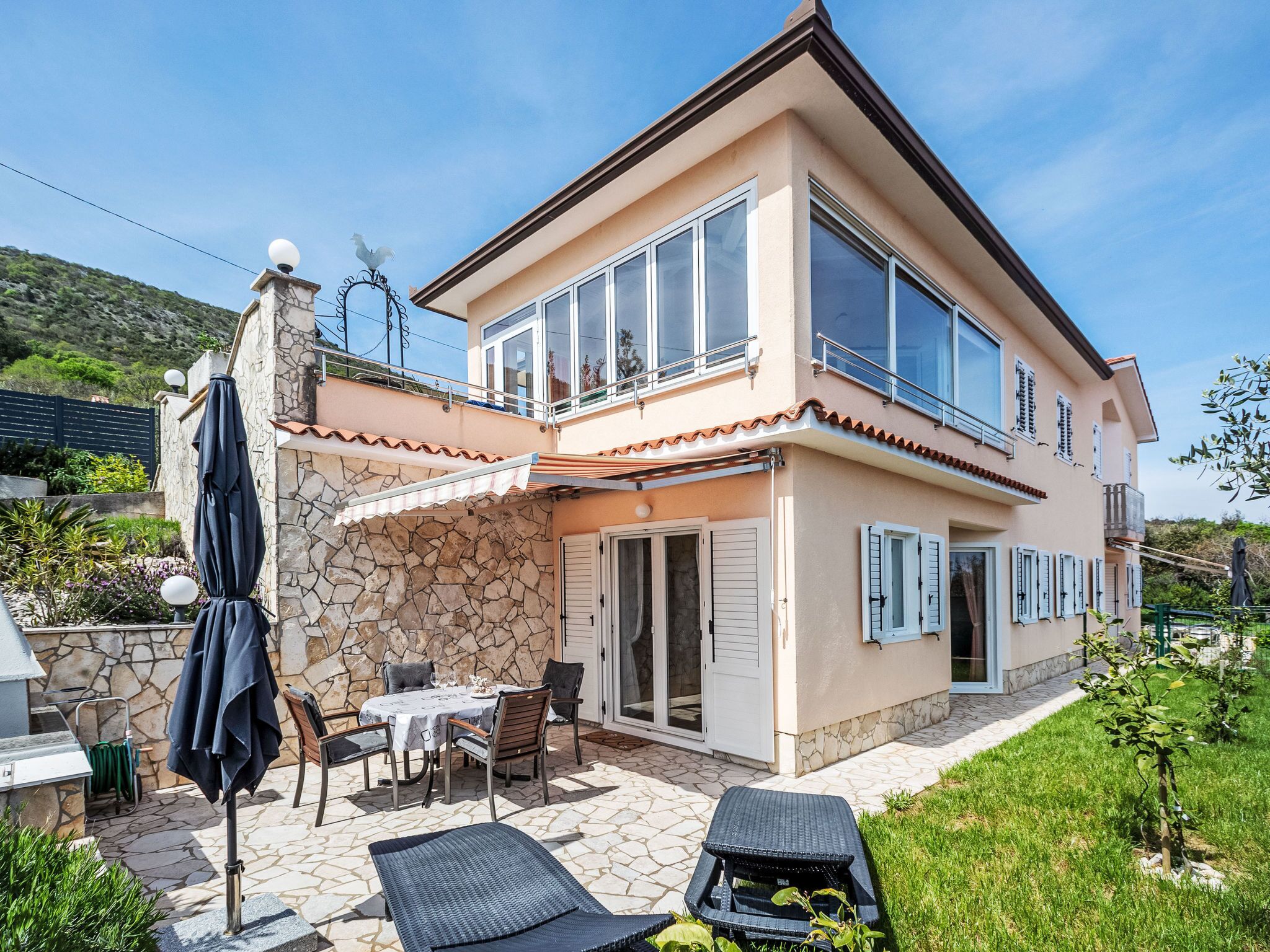 A two-story house with a stone facade, a balcony, and a patio with outdoor furniture.