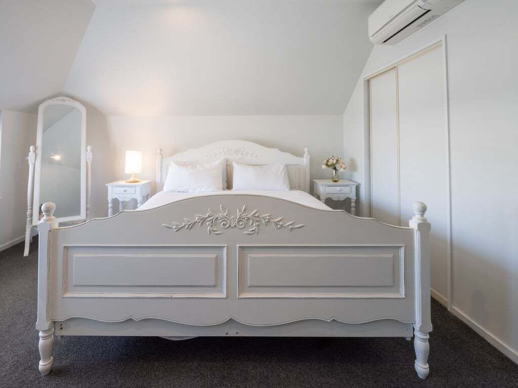 Un lit blanc, richement décoré, dans une pièce dotée d’un plafond en pente et d’un appareil de climatisation.