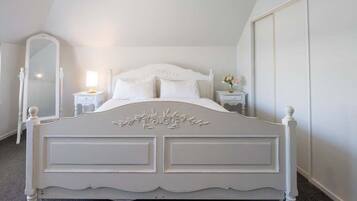 Un lit blanc, richement décoré, dans une pièce dotée d’un plafond en pente et d’un appareil de climatisation.