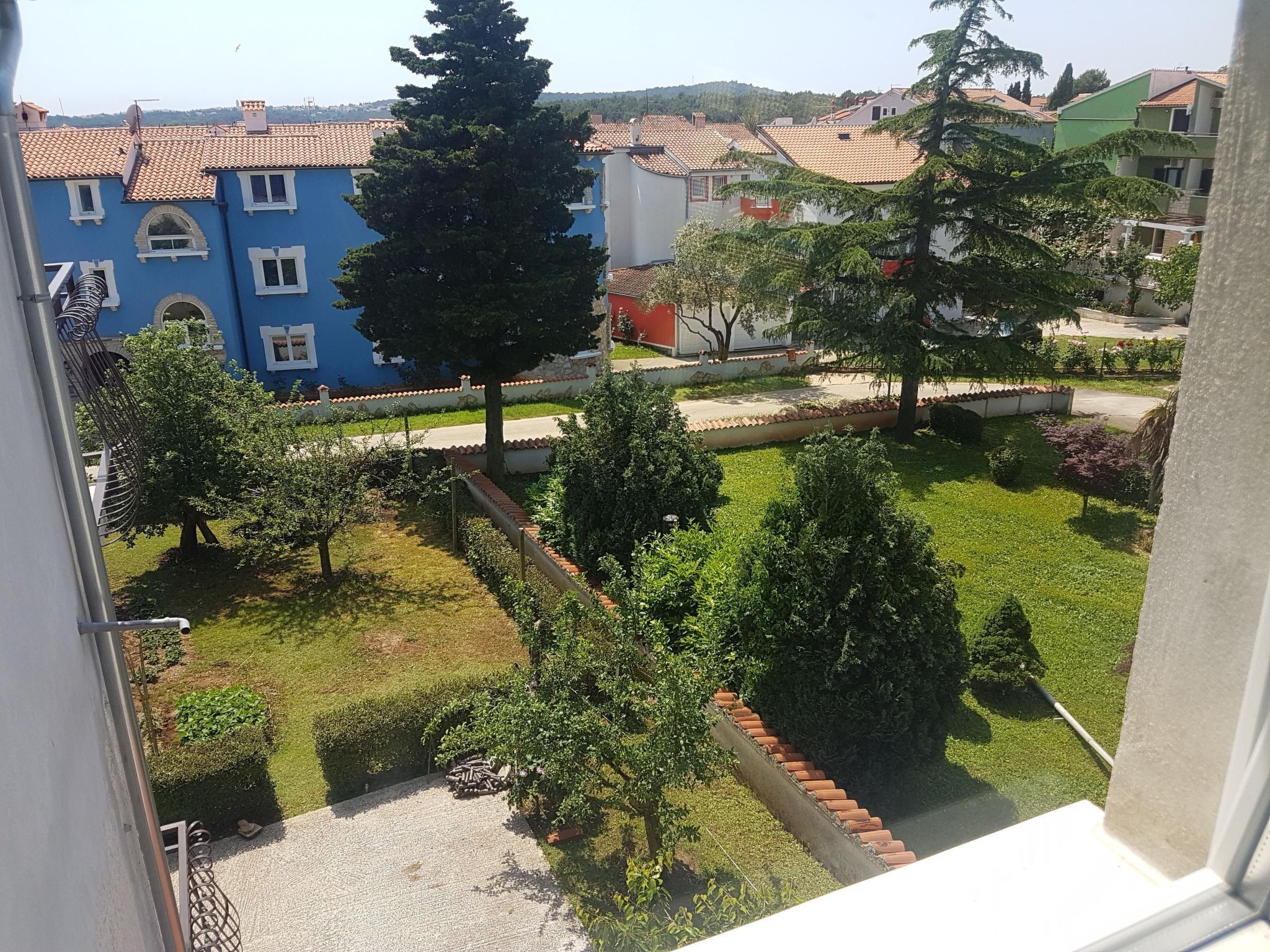Un quartiere residenziale con un edificio blu, un giardino con un vialetto lastricato e vista sulle case vicine.