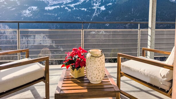 Een balkon met houten meubels en een vaas, met uitzicht op een bergachtig landschap.