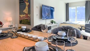 Een eetruimte met een houten tafel gedekt voor een maaltijd, een aan de muur bevestigde televisie en een schilderij van een vrouw in een jurk.