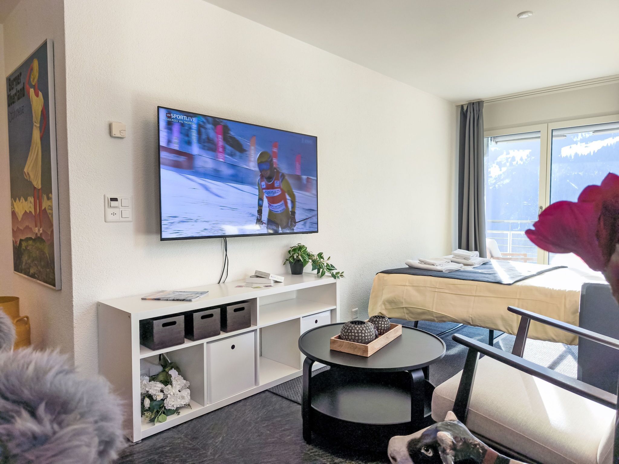 Una sala de estar moderna con un televisor de pantalla plana mostrando un evento deportivo, un sofá, una mesa de centro y una ventana con vistas al exterior.