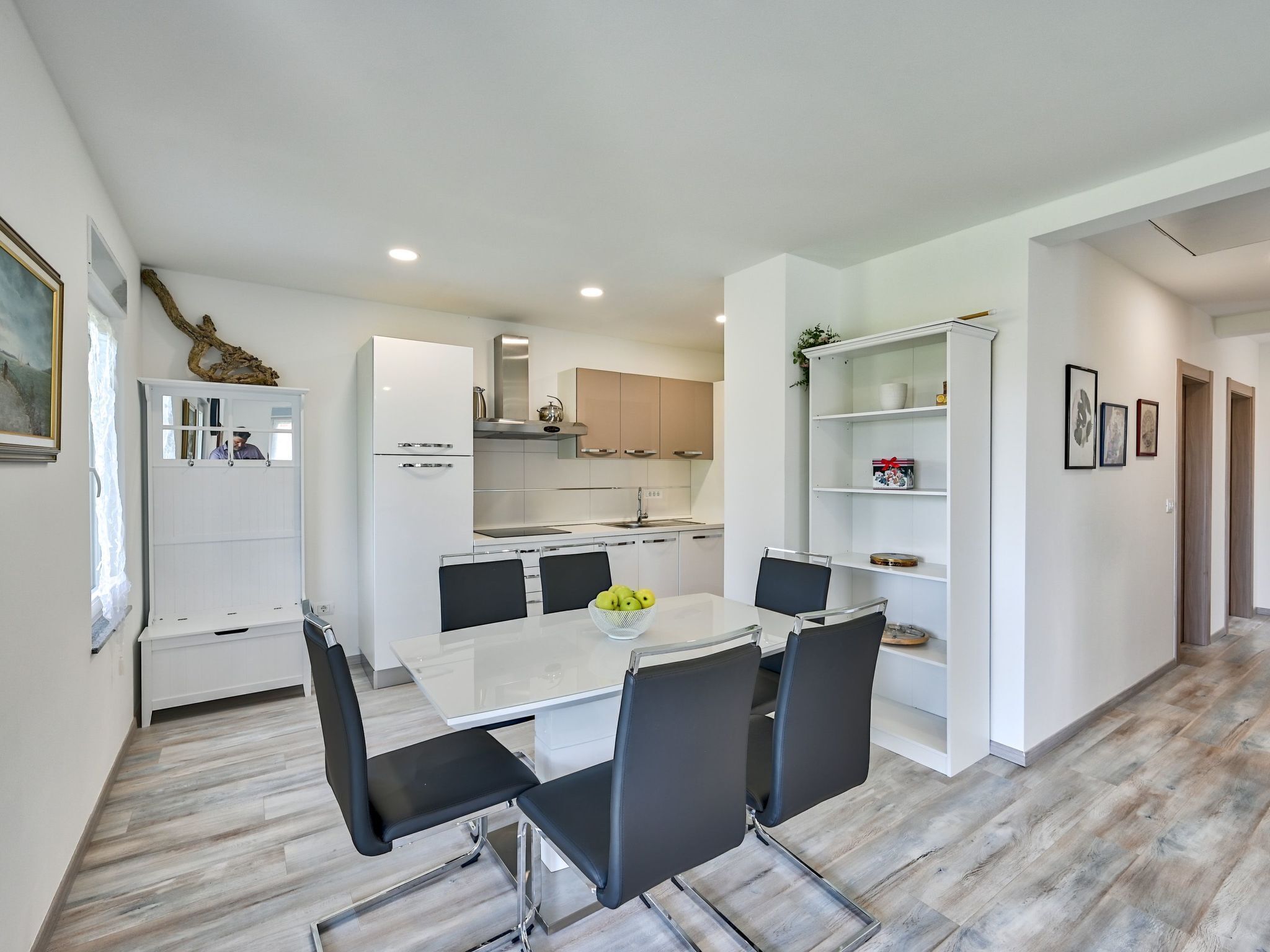 A modern kitchen with white cabinets, a central island, and a dining area with a white table and black chairs.