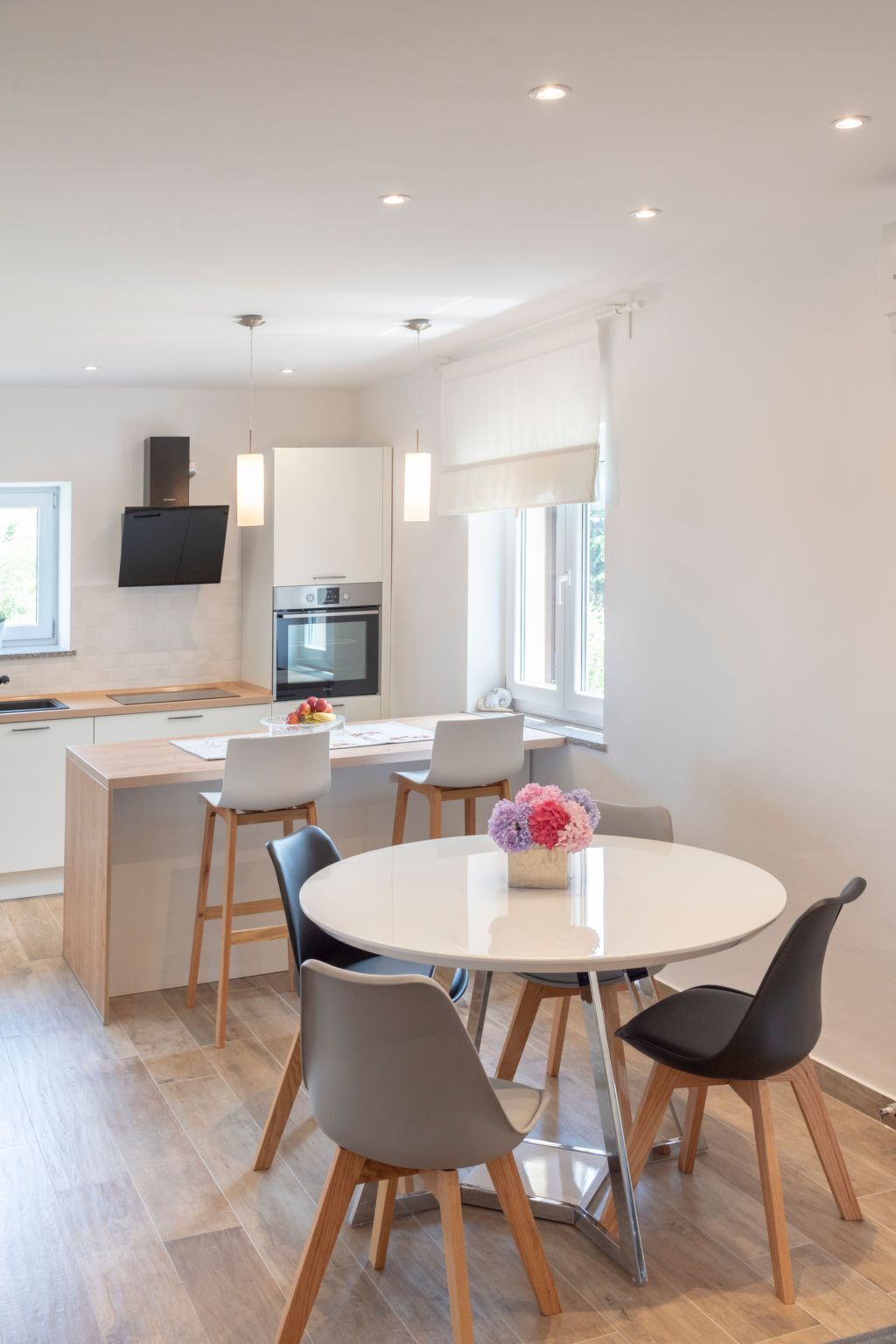 A modern kitchen with a built-in oven and a dining area with a round table and chairs.