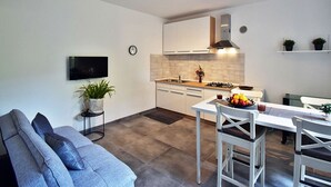 A modern kitchen with white cabinets, a built-in stove, and a dining area with a white table and chairs. - Wohnung a by Interhome (Fažana)