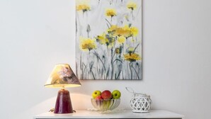 Un meuble blanc surmonté d’un saladier en verre rempli de fruits, d’une lampe et d’un objet décoratif.