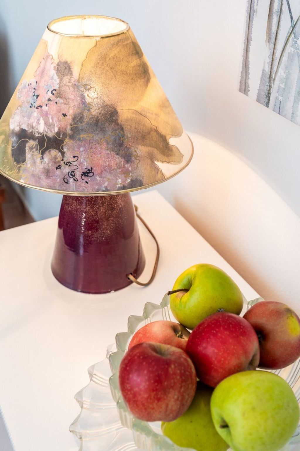 Un tavolo con una lampada decorativa e una ciotola di vetro piena di mele.