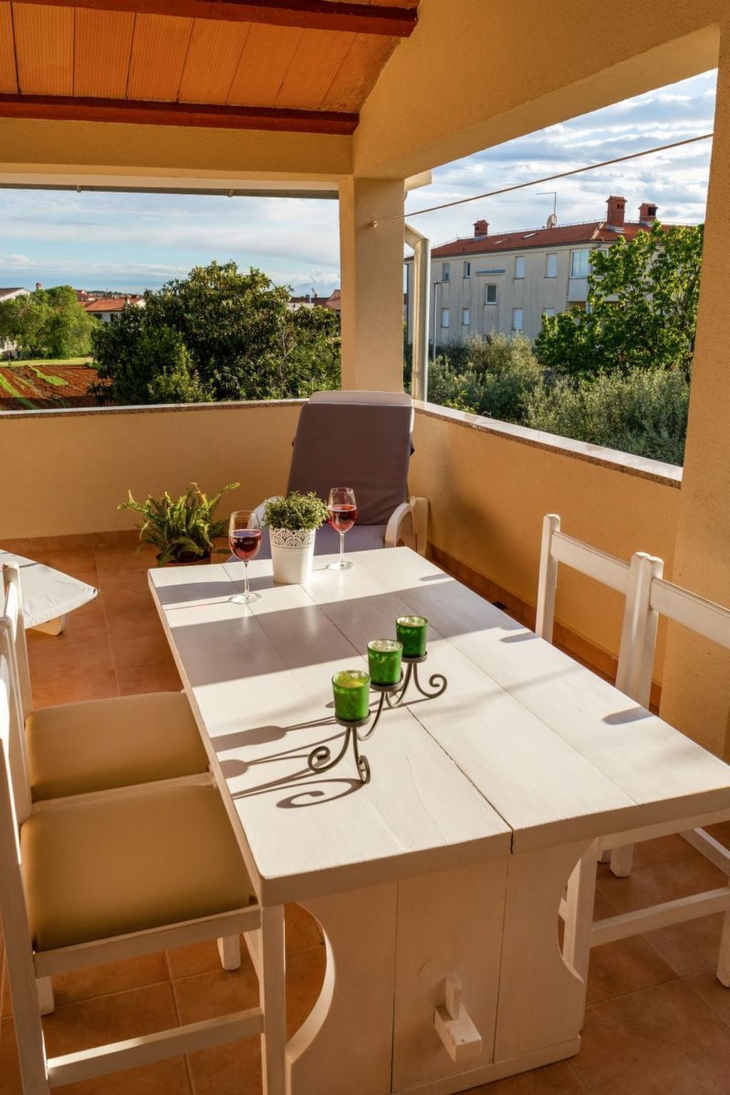 A balcony with a white table and chairs, a potted plant, and a glass of red wine.
