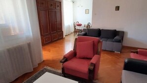 A living room with a red armchair, a grey sofa, and a white coffee table. There is a wooden cabinet and a dining area in the background. - Helle und luftige Ferienwohnung in erster Reihe zum Meer, mit einem privaten Ba by Interhome (Rovinj)