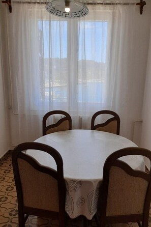 A dining area with a round table and four chairs, a chandelier, and a view of a body of water through sheer curtains. - Helle und luftige Ferienwohnung in erster Reihe zum Meer, mit einem privaten Ba by Interhome (Rovinj)