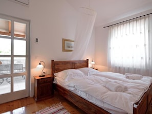 Una camera da letto con un letto di legno, due comodini con lampade, una finestra con tende leggere e vista sull'esterno.