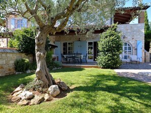 Una casa in pietra con patio, area salotto esterna e un grande albero nel giardino.