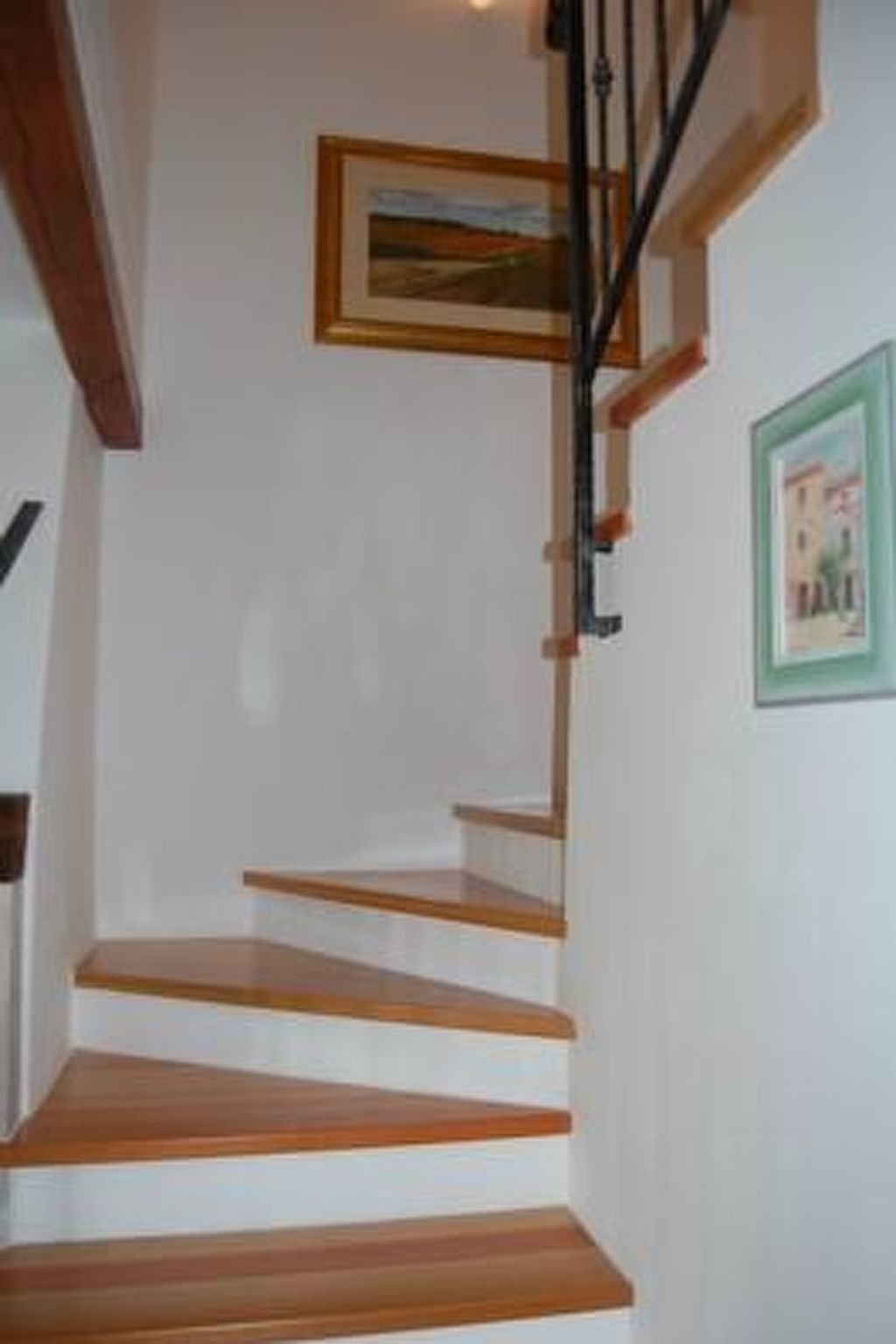 A staircase with wooden steps and a black handrail, leading to a landing with a framed picture on the wall.