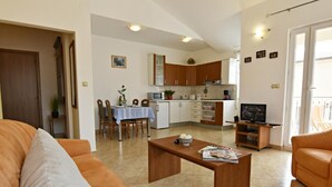 Un soggiorno con divano, tavolino e televisione. È presente una zona pranzo con tavolo e sedie. La cucina è visibile sullo sfondo.