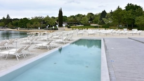Una piscina con lettini, cielo sereno e alberi sullo sfondo.