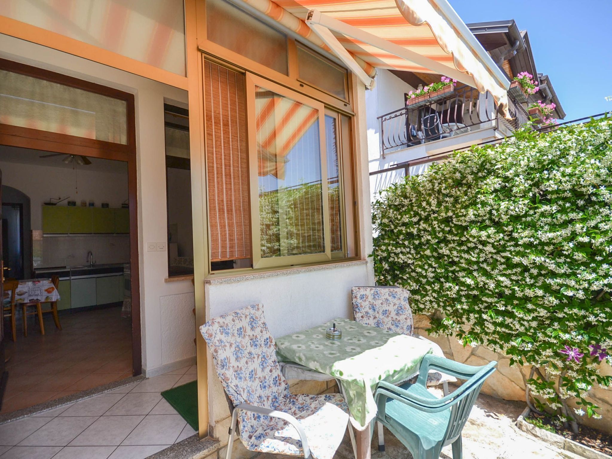 A patio with a table and chairs, a green bush, and a kitchen visible through an open door.