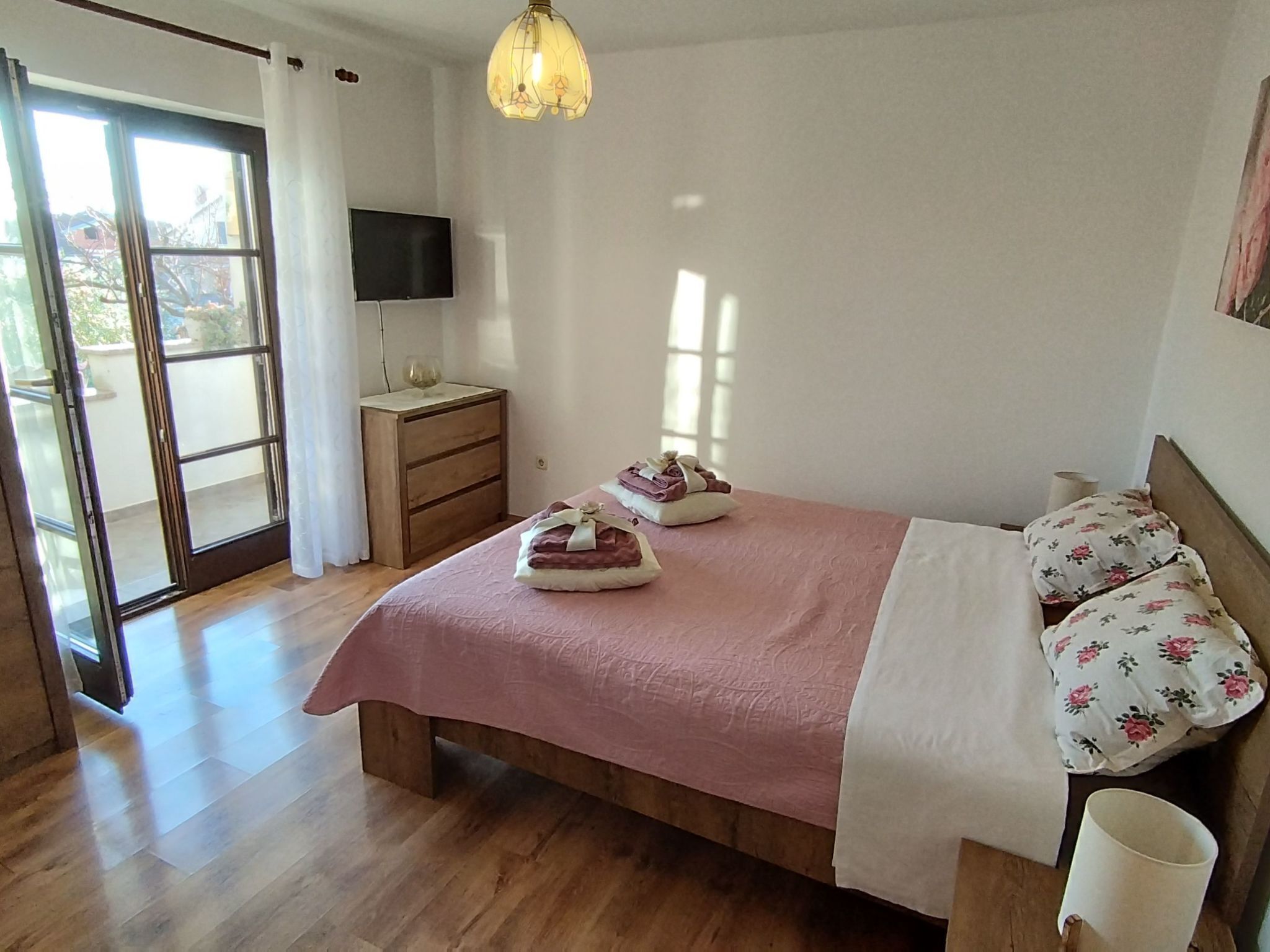 A bedroom with a bed, a nightstand, a TV, and a window.