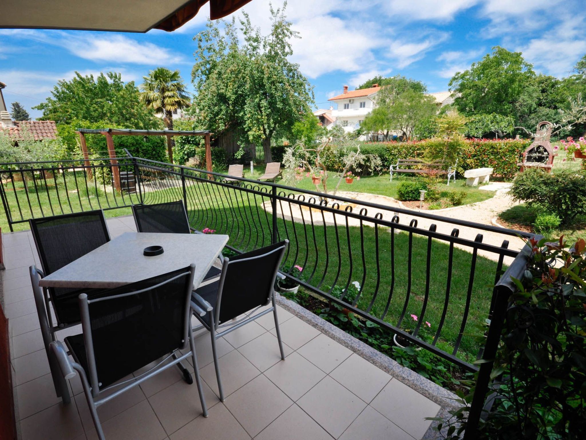 Ein Balkon mit Tisch und Stühlen, umgeben von einem Garten mit unterschiedlichen Pflanzen und einem Zaun.