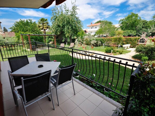 A balcony with a table and chairs, surrounded by a garden with various plants and a fence.