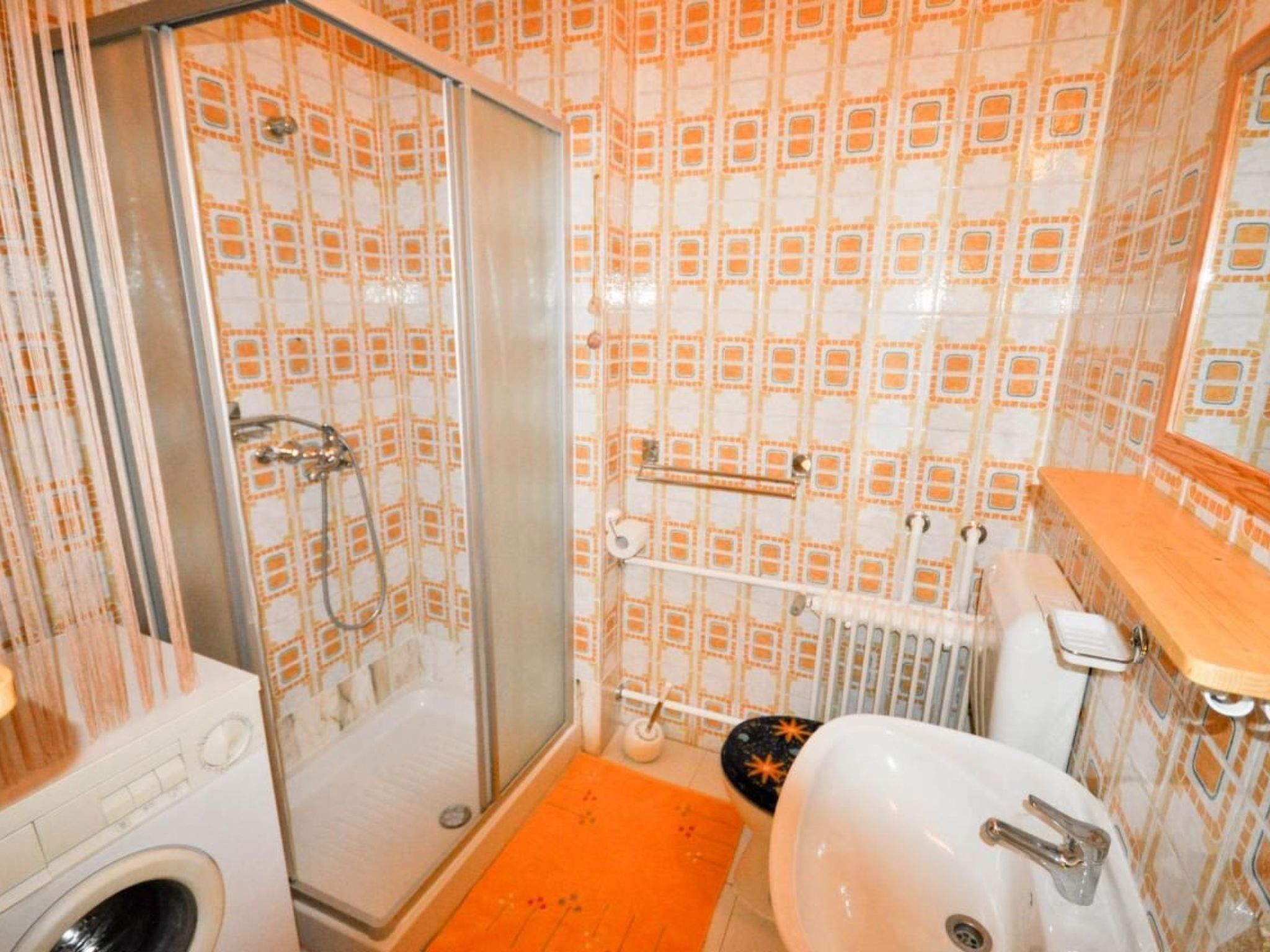 Casa de banho com chuveiro, sanita, lavatório e máquina de lavar roupa.