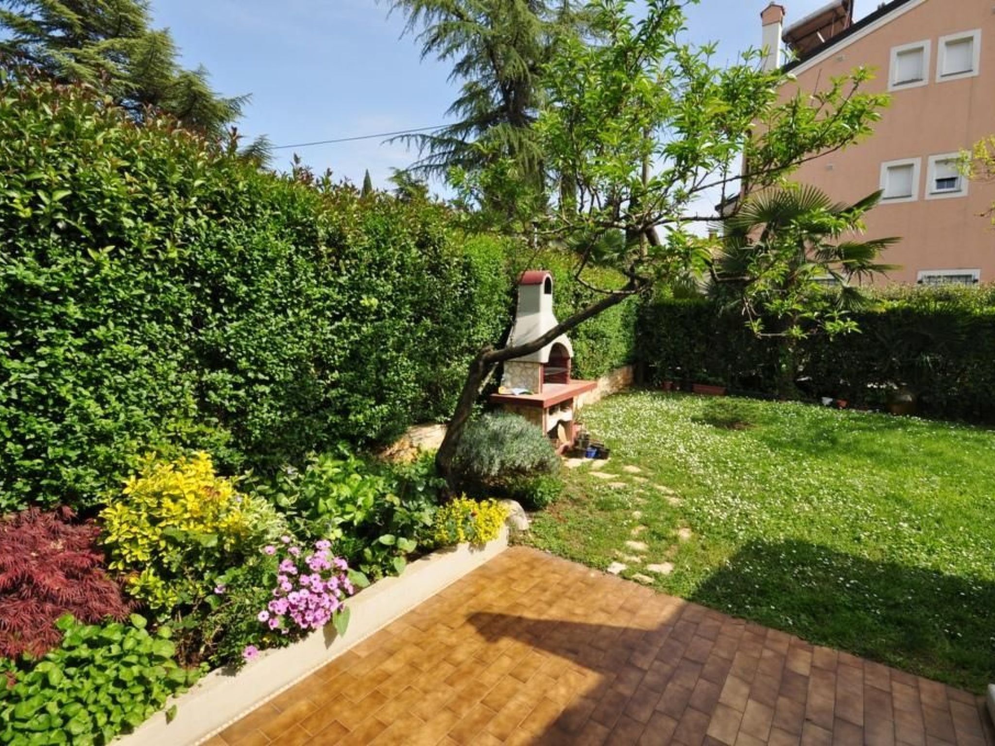 A well-maintained garden with a brick patio, various shrubs, and a small outdoor grill area.