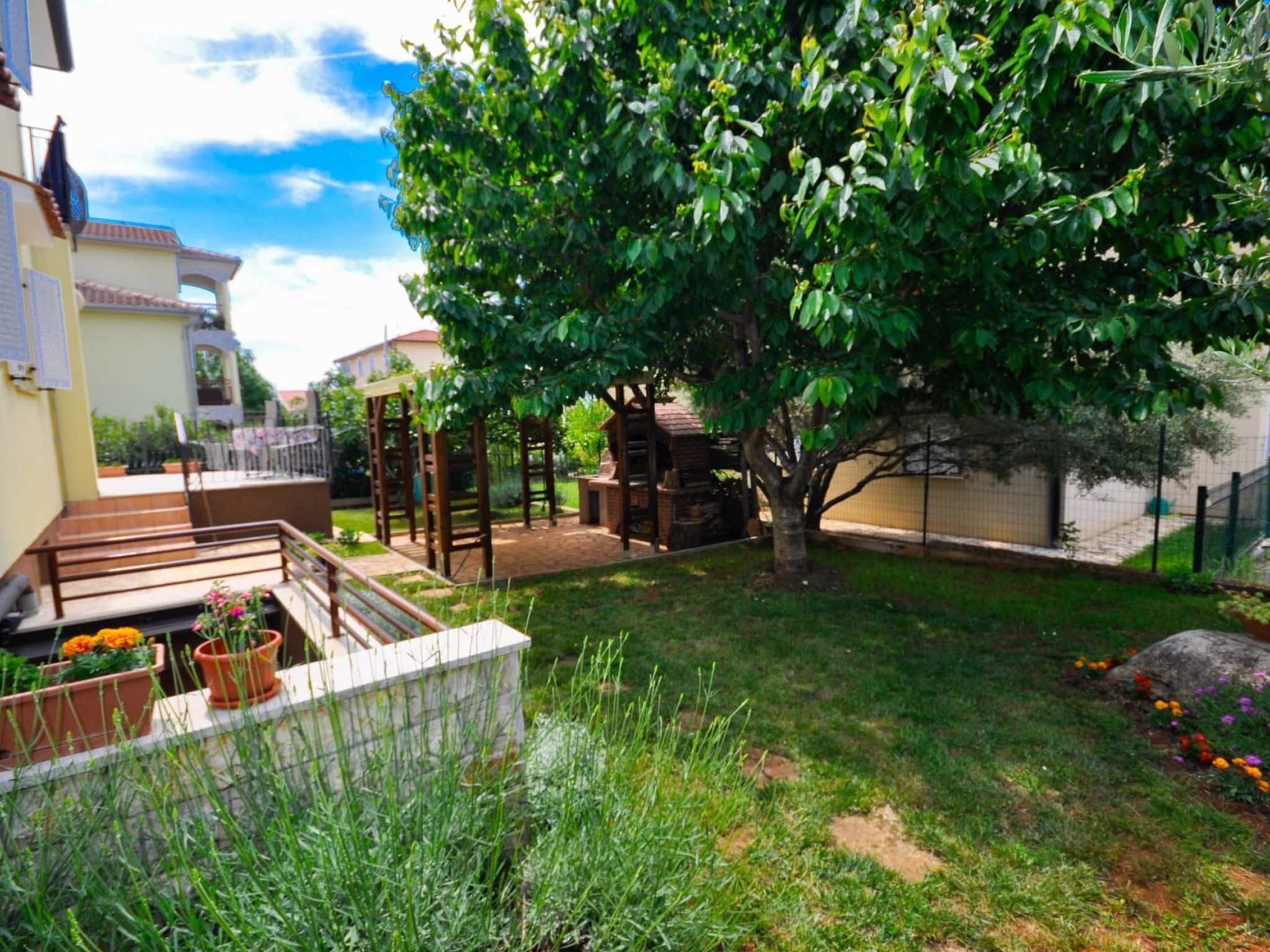 Un jardin à l’arrière de la maison, agrémenté d’une pergola, d’un espace barbecue et d’un petit potager fleuri.