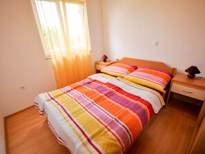 A bedroom with a wooden bed, striped bedding, a nightstand with a lamp, and a window with curtains. - für 2 Personen 35 m2 in Novigrad, Istrien by Interhome (Novigrad (Istra))