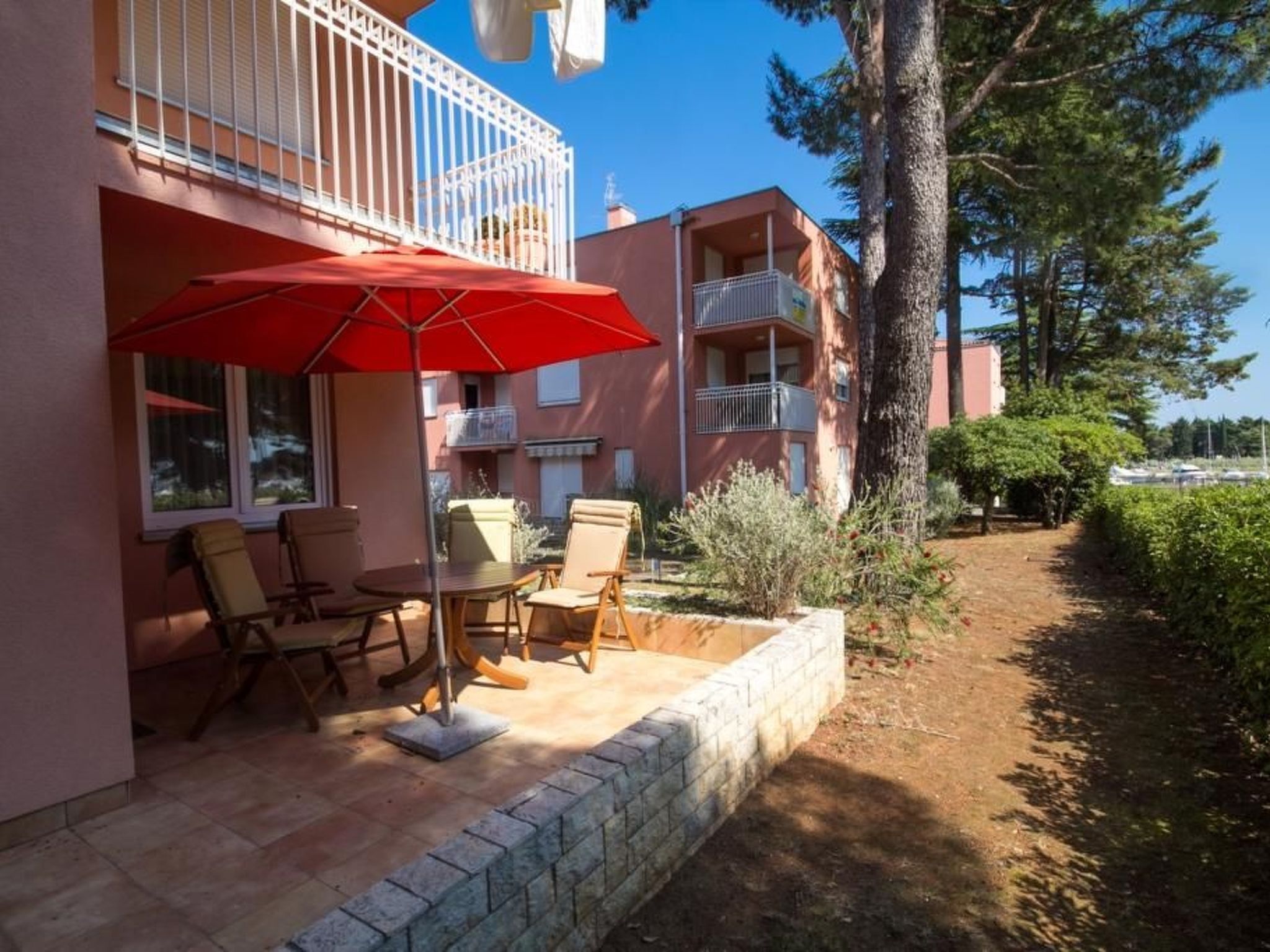 A patio with outdoor furniture and a red umbrella, surrounded by a brick wall and a small garden.