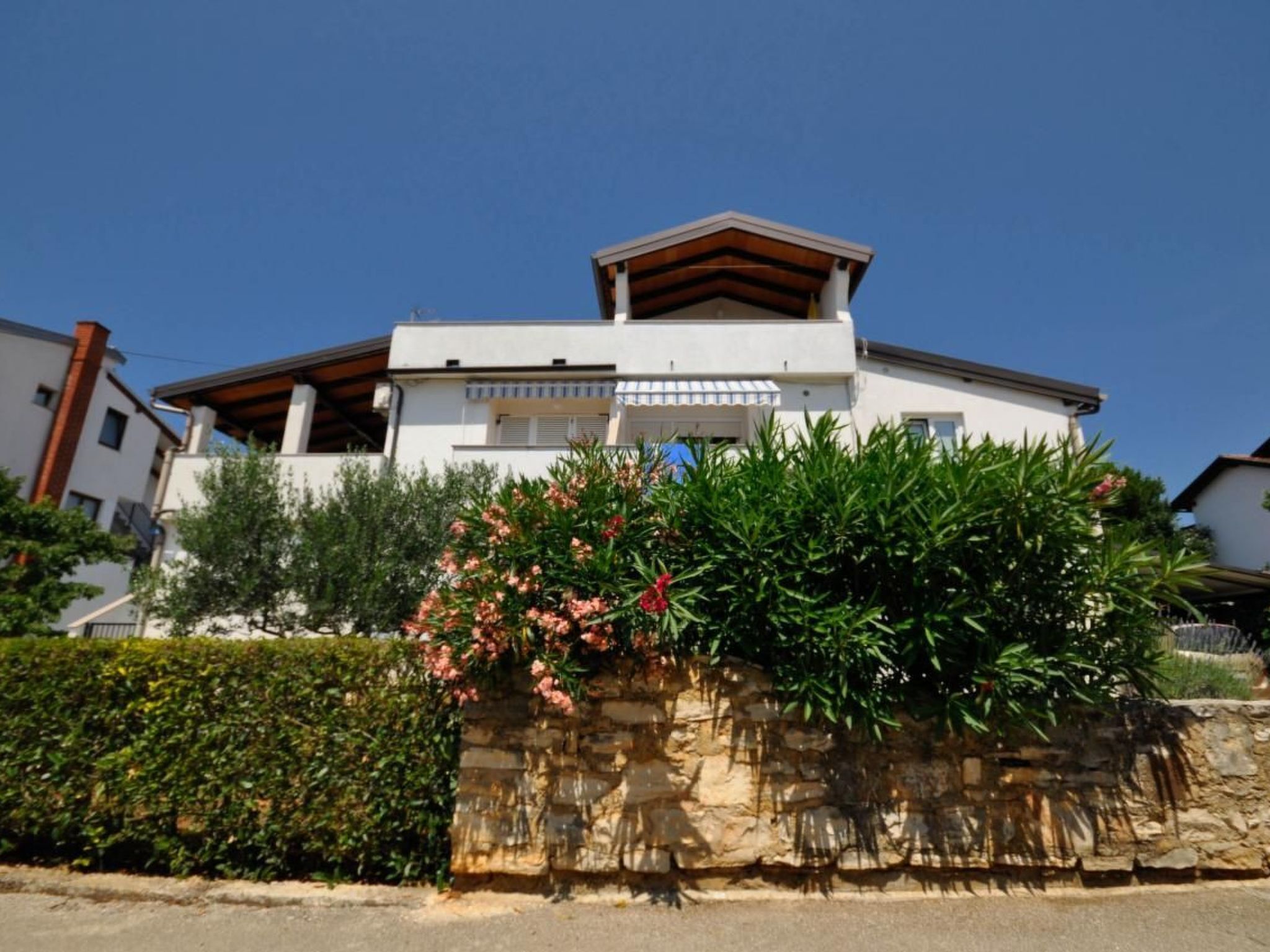 Uma casa moderna de dois andares com uma parede de pedra e uma pérgula de madeira.