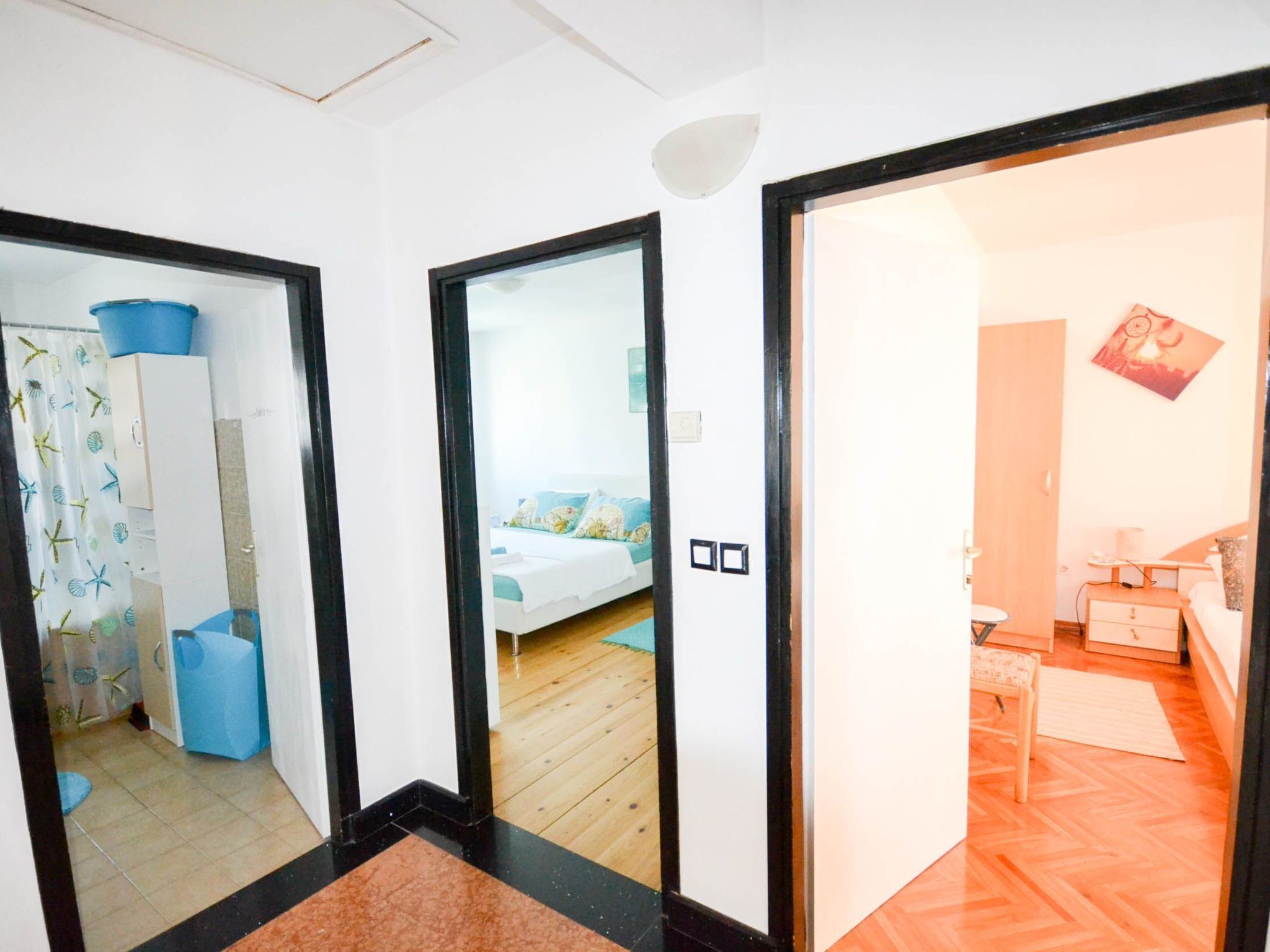 A hotel room with a bed, a desk, and a chair. There is a bathroom with a sink and a mirror. The room has a wooden floor and white walls.
