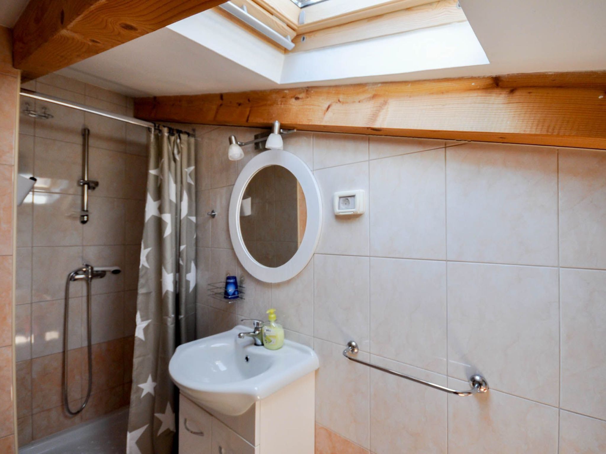 Une salle de bain avec un puits de lumière, une douche, un lavabo et un miroir.