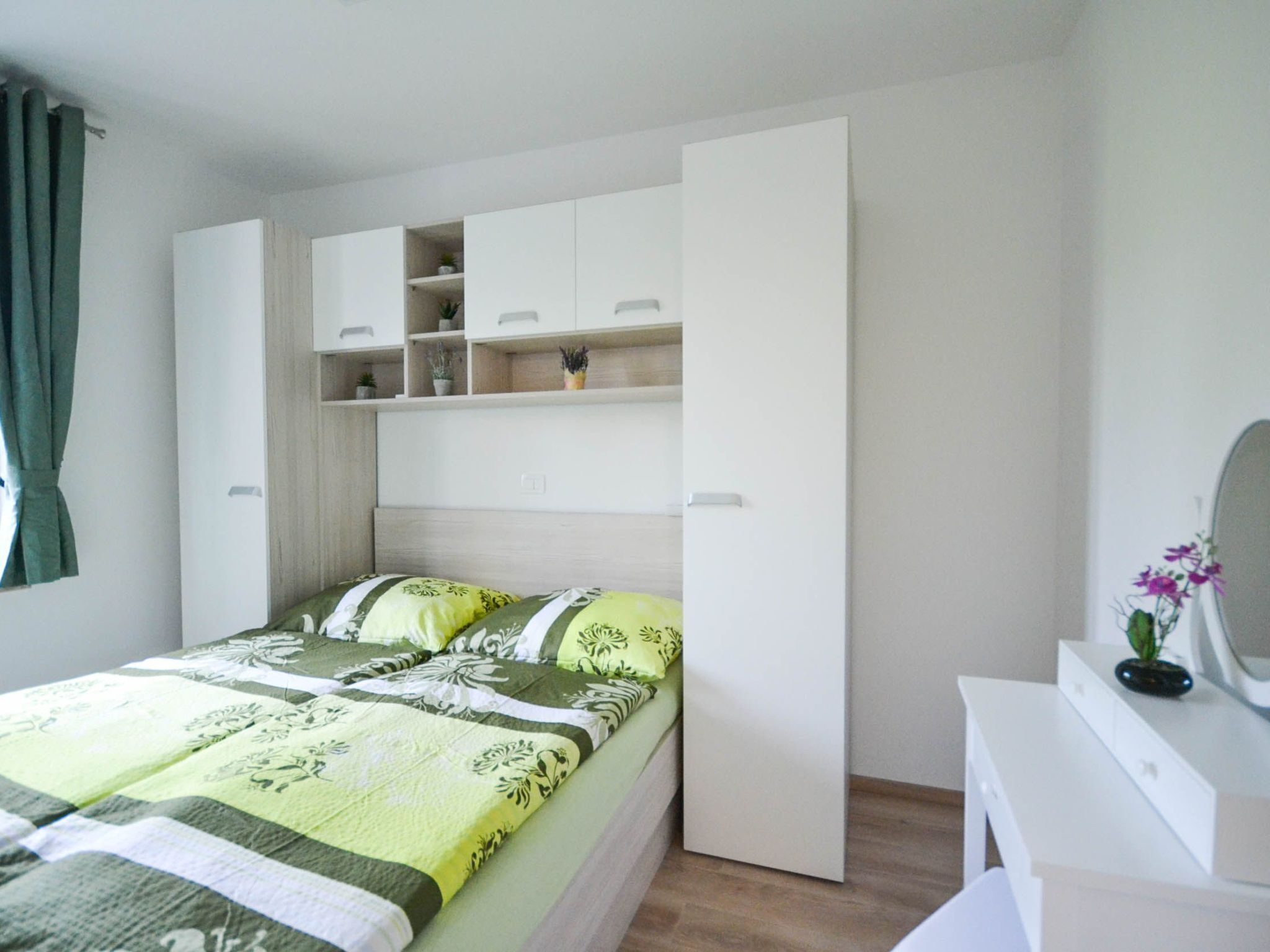 A bedroom with a bed, a white dresser, and a built-in shelving unit with potted plants.