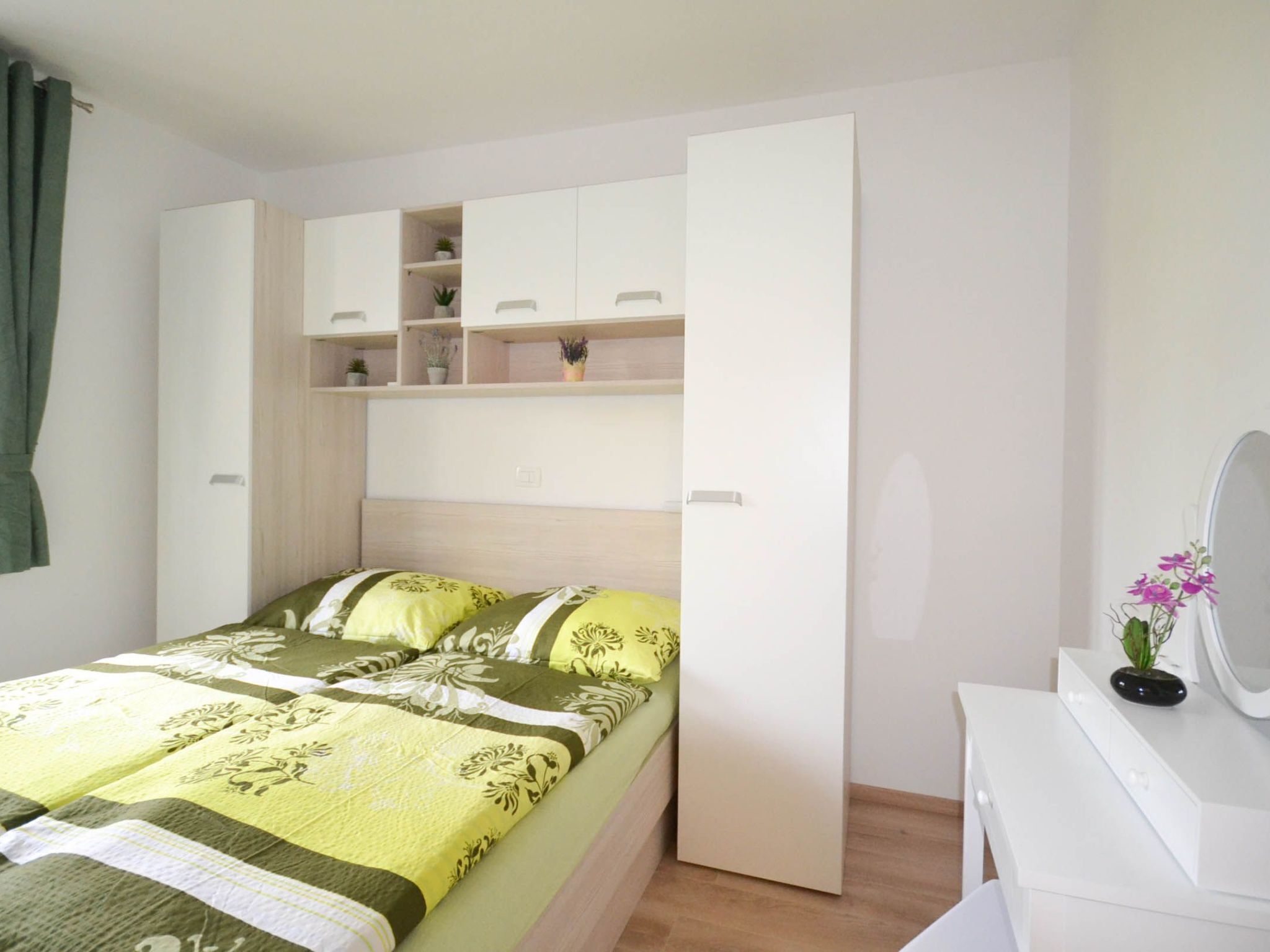 A bedroom with a bed, a white dresser, and a built-in wardrobe with shelves.