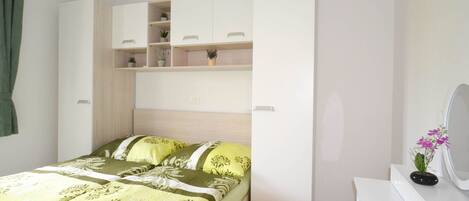 A bedroom with a bed, a white dresser, and a built-in wardrobe with shelves.