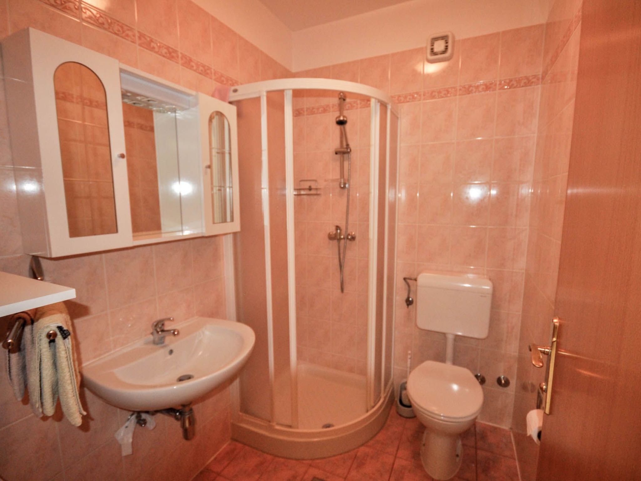 A bathroom with a curved shower enclosure, a sink, a toilet, and a mirror above the sink.